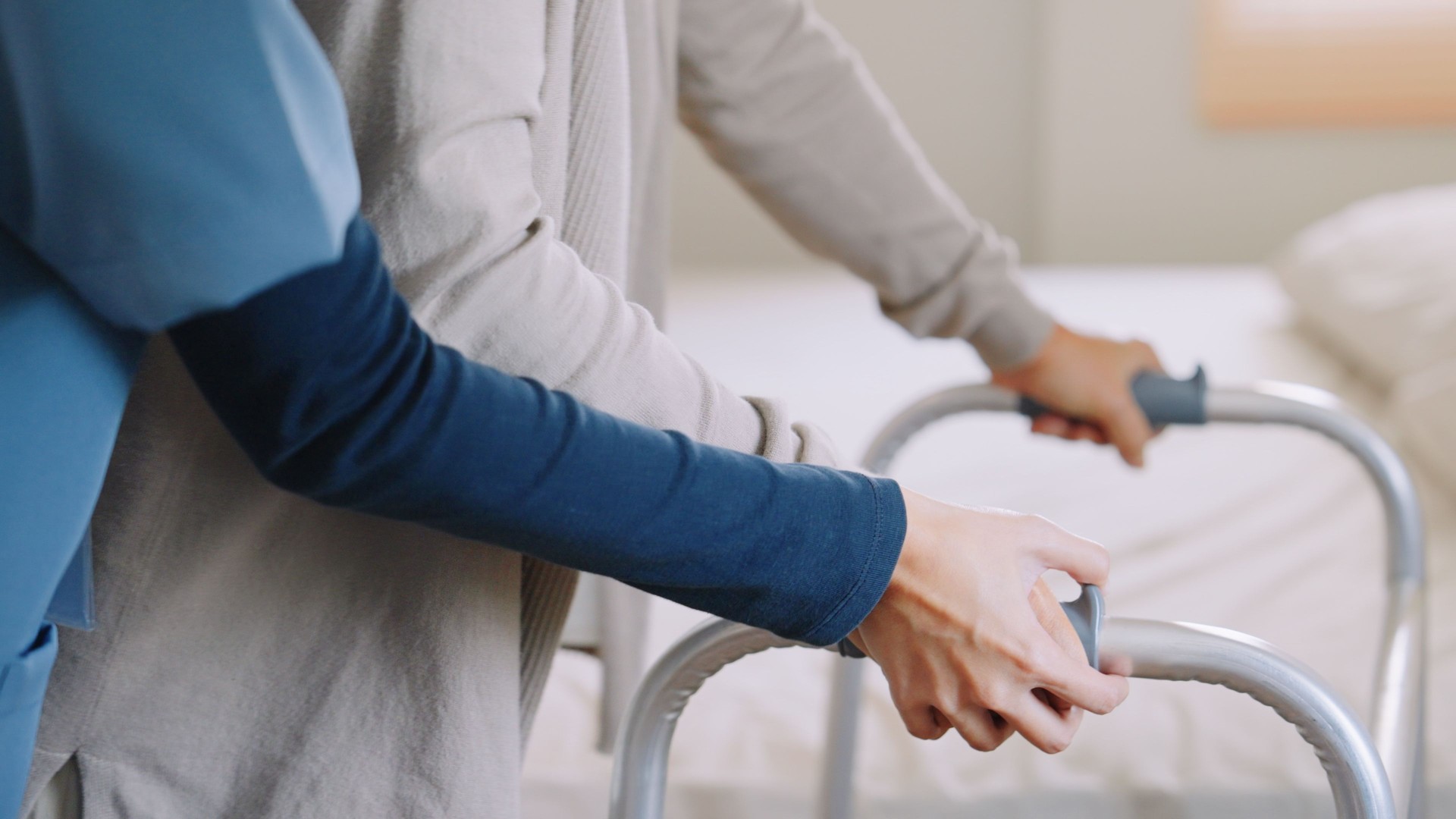 Asian woman caregiver nurse wearing blue scrubs assisting an elderly woman retirement using a mobility worker The healthcare worker helping stand up transition from mobility worker to bed relaxing  support  for wellbeing and be a healthy lifestyle Medical